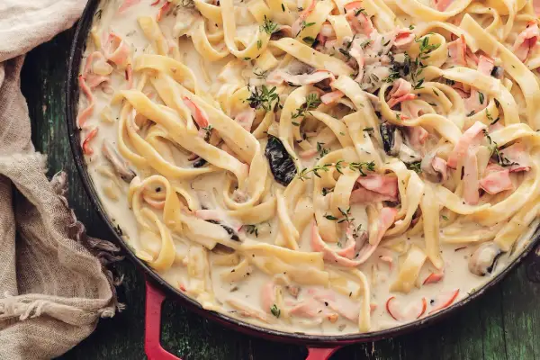 Tagliatelle w kremowym sosie z kawałkami szynki i grzybów, pachnące tymiankiem. Pyszne mac and cheese w nowej odsłonie.