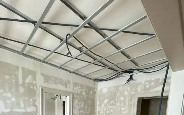 Structure métallique pour faire un faux plafond, avec des câbles électriques en cours d'installation. Les murs sont en chantier.
