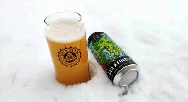 Szklanka piwa z logo "Trzech Kumpli" i puszka "Like a Forest" od **browaru Nepomucen** w śniegu.