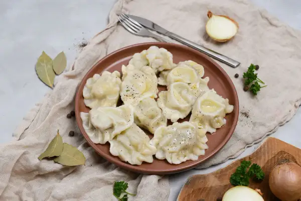 Smażone pierogi z mięsem na brązowym talerzu, z cebulą i natką pietruszki w tle.
