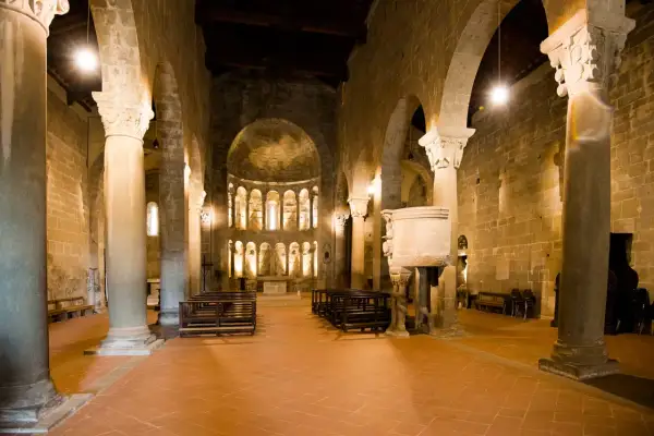 Interno della pieve di Gropina, con colonne massicce, archi in pietra, un pulpito scolpito e l'abside illuminata.