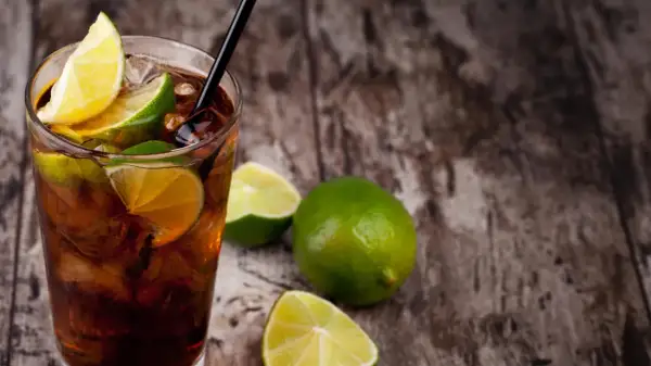 Erfrischender Cuba Libre mit Limettenspalten und Eiswürfeln auf rustikalem Holz. Das Cuba Libre Rezept ist einfach und lecker.