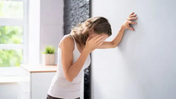 Frau lehnt sich an Wand, hält sich die Augen. Sie fragt sich, was tun bei Schwindel.