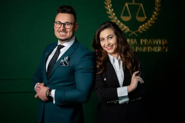 Para prawników w eleganckich garniturach na tle zielonej ściany z logo kancelarii.