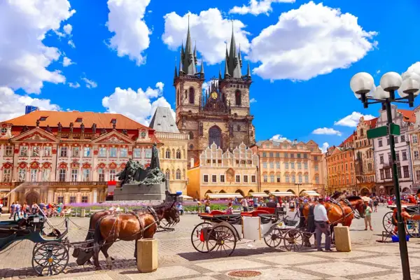 Rynek w Pradze z kościołami, kamienicami i dorożkami konnymi.