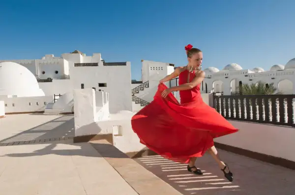 Bailarina con vestido rojo gira con gracia, evocando la pasión de los flamencos de Jerez bajo un cielo azul.