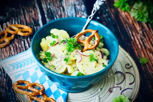 Klassisches Rezept Kartoffelsalat mit roten Zwiebeln und Petersilie, garniert mit einem Brezel.