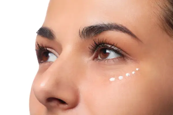 Application de crème hydratante en points sur le coin interne de l'œil pour un maquillage lumineux.