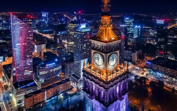 Wieżowiec z zegarami i nowoczesne budynki tworzą magiczny krajobraz warszawa nocą.