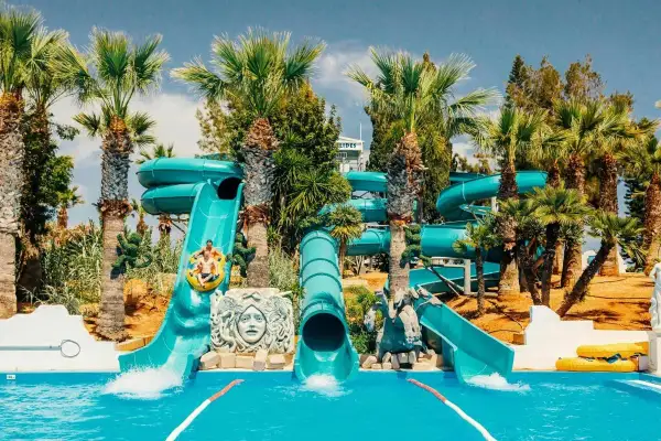 Vattenrutschkanor i Waterworld Ayia Napa med palmer och sol. Två personer åker i en ring nerför en blå vattenrutschkana.