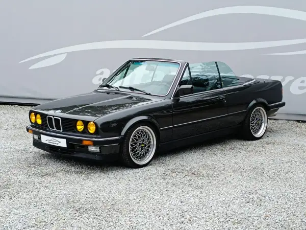 Czarny kabriolet BMW E30 z żółtymi światłami i felgami BBS. Klasyk na drodze.