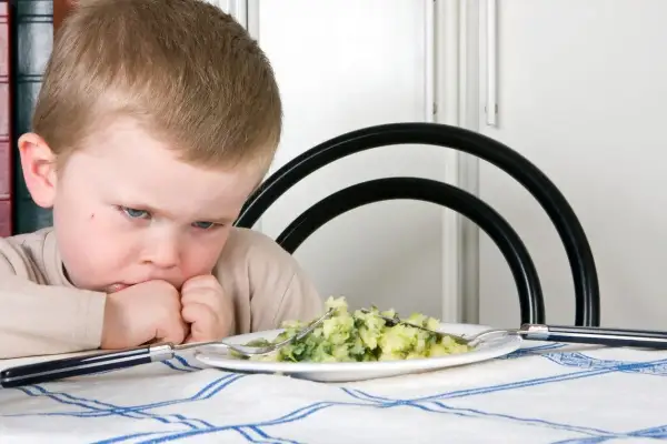 Bambino con espressione di disgusto davanti a un piatto di purè e verdure. Il suo volto mostra un riflesso di estrusione, come se volesse fuggire da quel cibo.