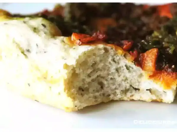 Gros plan sur une tranche de pâte à pizza sans gluten moelleuse, garnie de tomates et d'herbes.