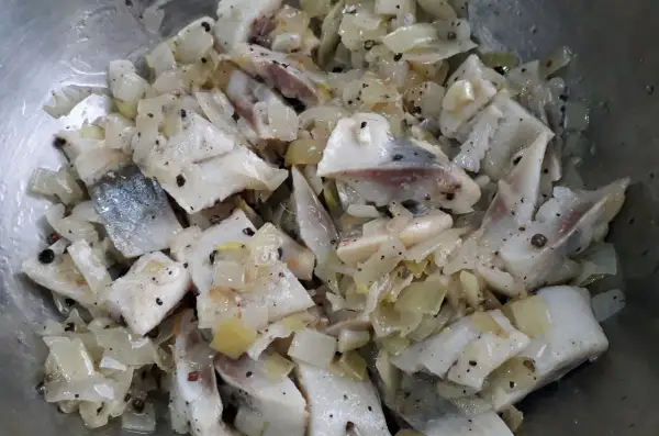 Pokrojone śledzie w oleju z cebulą i pieprzem, gotowe do podania.