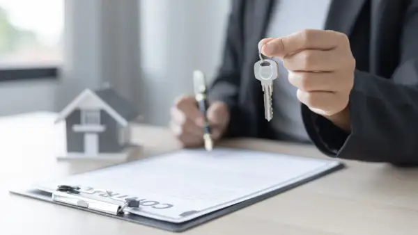 Persona firma un contrato de alquiler con opción a compra, sosteniendo la llave de una casa en miniatura.