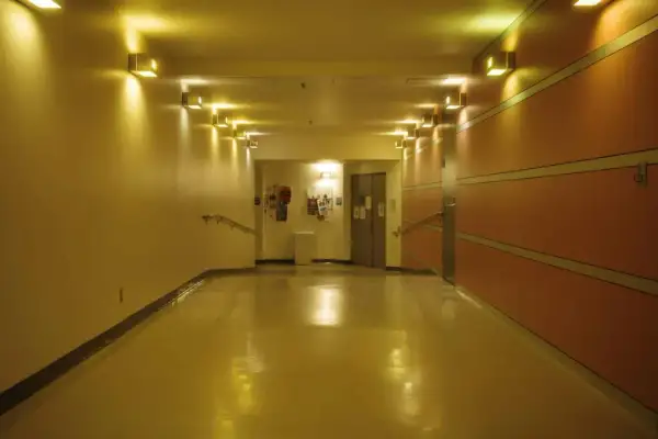 Korytarz z żółtym, błyszczącym podłogą i rzędem lamp. Oświetlenie awaryjne zapewnia bezpieczeństwo.