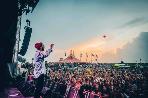 Bühnenkünstler wirft roten Ball in die Menge beim Watt en Schlick Festival Dangast. Ein Meer aus Menschen feiert unter dem Abendhimmel.