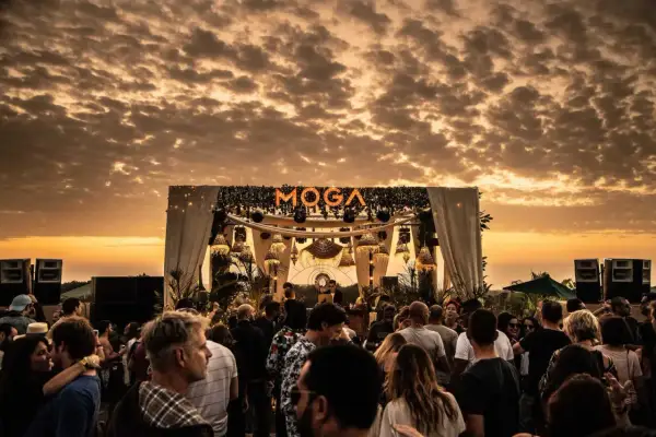 Multitud disfrutando del atardecer en el moga festival, con luces y escenario decorado.