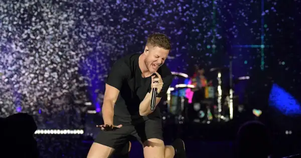 Imagine Dragons wokalista Dan Reynolds śpiewa z pasją na scenie, otoczony konfetti.
