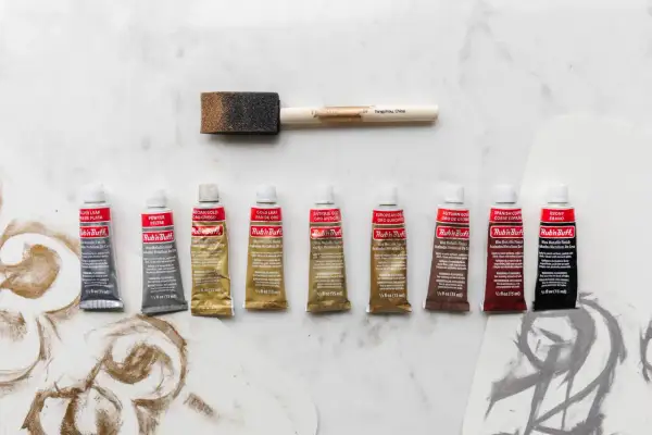 A collection of Rub'n Buff wax metallic finish tubes in various colors, alongside a foam applicator brush, ready to add a beautiful sheen to any project.