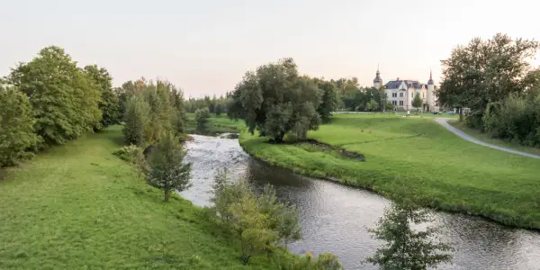 Idyllischer Flusslauf mit grünen Ufern und einem Schloss im Hintergrund. Ein perfekter Ort für Radwege Geheimtipp-Touren.
