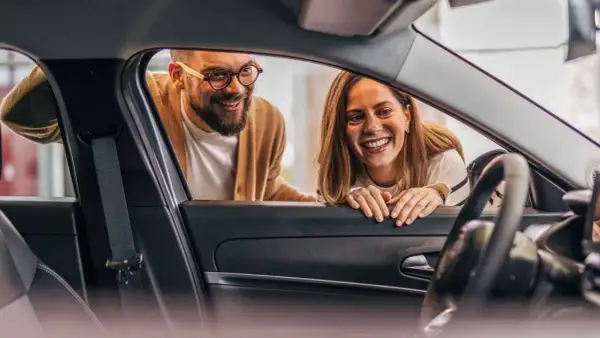 Ett leende par tittar in i en ny bil. De funderar på hur funkar privatleasing för att få sin drömbil.