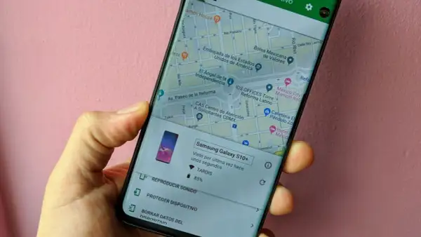 Mano sujetando un móvil que muestra la función de localizar móvil. Se ve un mapa de la Ciudad de México y opciones para reproducir sonido o proteger el dispositivo.