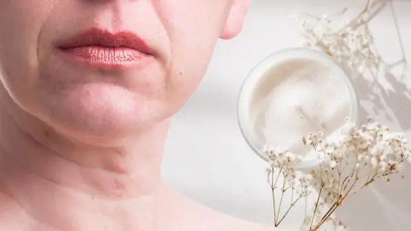 Un vasetto di crema e fiori secchi accanto al viso di una donna, suggerendo come migliorare la pelle del viso con prodotti naturali.