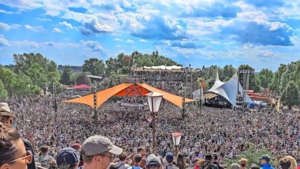 Tausende feiern auf dem Fusion Festival Ort unter blauem Himmel. Bunte Zelte und Bühnen prägen die Szenerie.