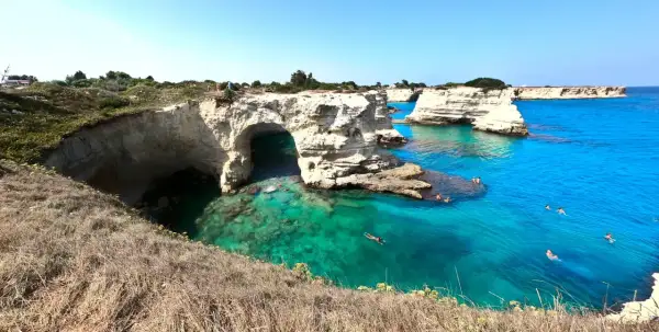 Scogliere bianche e mare cristallino nel Salento, con persone che nuotano e si godono il sole.