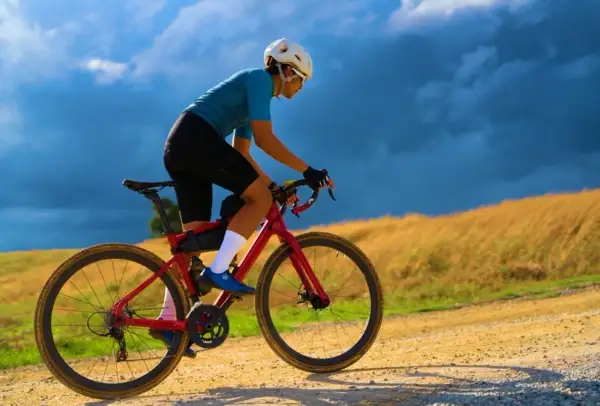 Kobieta w kasku i sportowym stroju pokonuje szutrową trasę na czerwonym rowerze gravel.