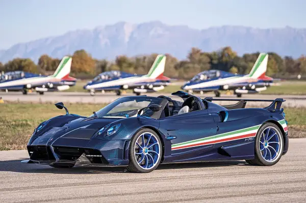 Niebieski Pagani Huayra Roadster z włoską flagą na boku, obok samolotów akrobacyjnych. Jego pagani huayra cena jest astronomiczna.