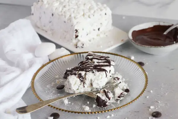 Una fetta di meringata al cioccolato, soffice e golosa, con scaglie di cioccolato e una cascata di salsa al cacao.