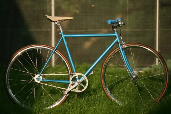 Błękitny rower ostre koło z brązowymi oponami i siodełkiem, gotowy na miejskie wyzwania.