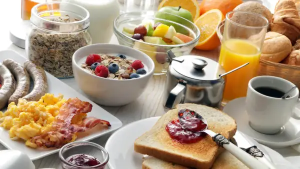 Ein reichhaltiges Frühstück in Görlitz: Rührei, Speck, Würstchen, Müsli, Obst, Toast mit Marmelade, Saft und Kaffee.