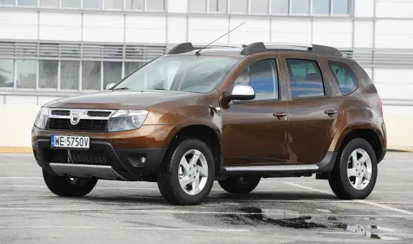 Brązowy Dacia Duster na parkingu, gotowy do testu. Widoczny kierowca za kierownicą.