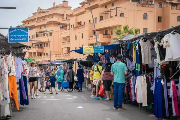 Gente comprando ropa en puestos del paseo marítimo de Garrucha. Edificios naranjas al fondo.