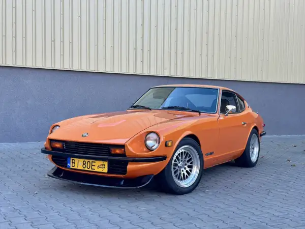Pomarańczowy Datsun 280Z z lat 70. na tle budynku. Klasyk motoryzacji gotowy na przejażdżkę.