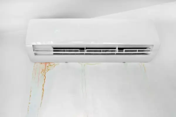 Condizionatore che perde acqua, lasciando macchie umide e colorate sul muro bianco.
