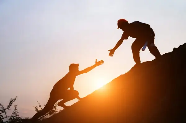 Siluetas de dos hombres ayudándose a subir una colina al atardecer. Un gesto de apoyo que contrasta con las frases de invalidación emocional.