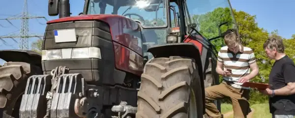 Zwei Männer besprechen den Einsatz eines Traktors. Der jüngere schaut aufs Handy, der ältere hält eine Mappe. Ein guter Verdienst als Fachkraft Agrarservice ist wichtig.