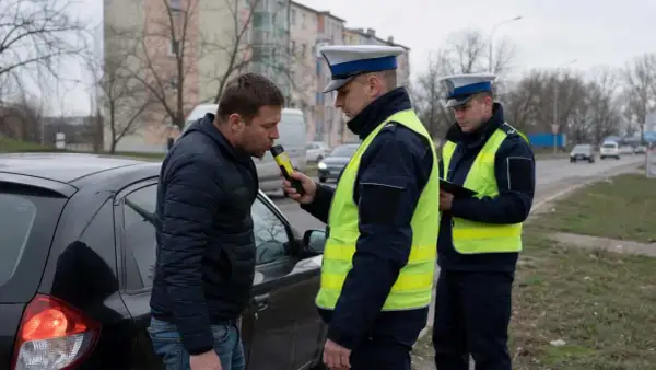 Policjant bada kierowcę alkomatem. Kontrola drogowa ma zapobiec jeździe pod wpływem alkoholu.