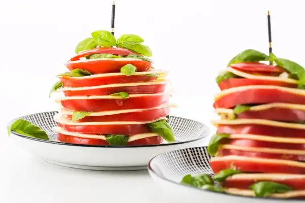 Torres de tomates y mozzarella con albahaca, unos entrantes típicos de Francia, servidos en platos con diseño geométrico.