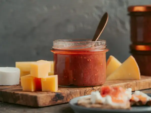Glas mit rotem Chutney, daneben Käsewürfel und -stücke. Perfekt für leckere Chutneys Rezepte.