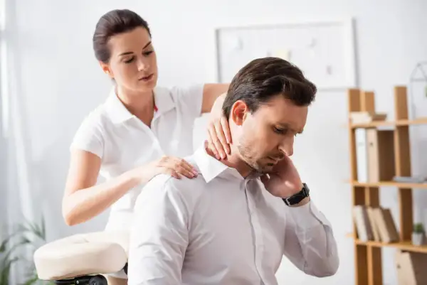 Une thérapeute prodigue un massage au bureau à un homme d'affaires, soulageant ses tensions au cou et aux épaules.