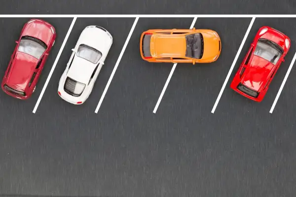 Cztery samochodziki na parkingu, gotowe do równoległego parkowania. Czerwony, biały, pomarańczowy i znów czerwony.