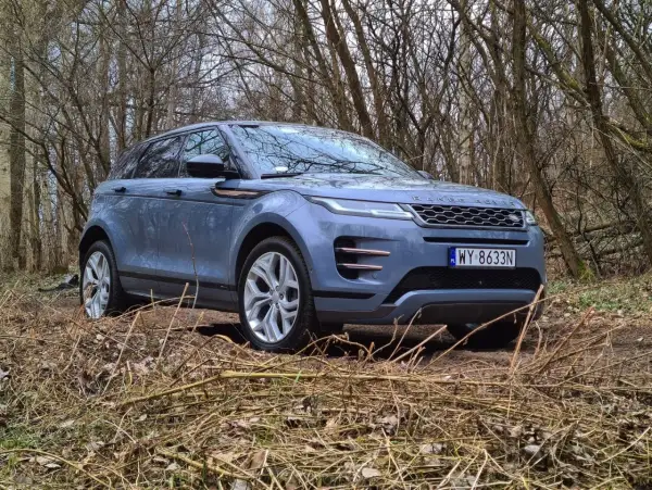 Niebieski Land Rover Evoque wjeżdża w leśną ścieżkę, otoczony suchymi gałęziami i drzewami.