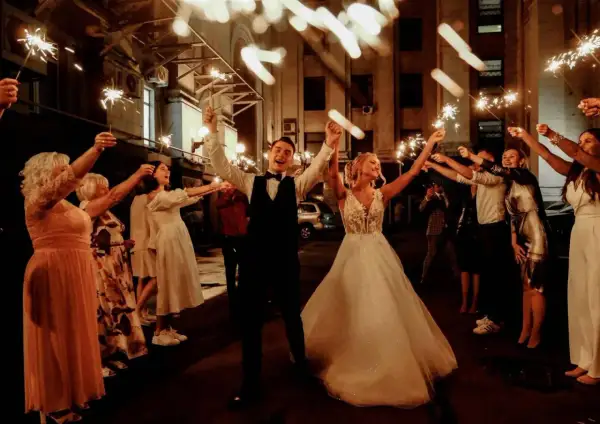 Un couple de mariés rayonnant, entouré d'invités tenant des feux de Bengale, pour un thème mariage étoile scintillant.