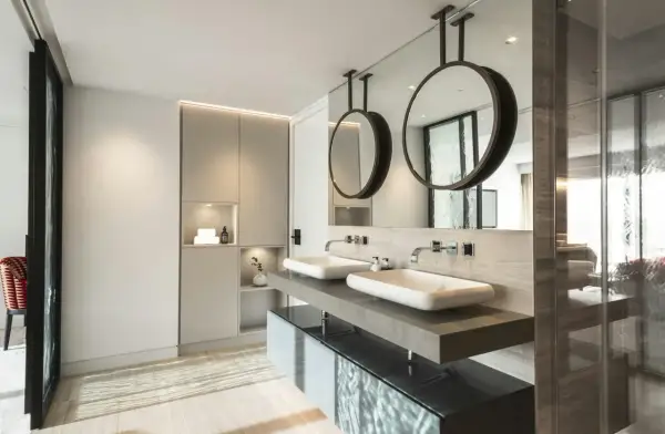 Un moderno baño con dos lavabos sobre encimera de piedra, espejos circulares colgantes y armarios integrados. Se puede hacer un baño en una habitación así.