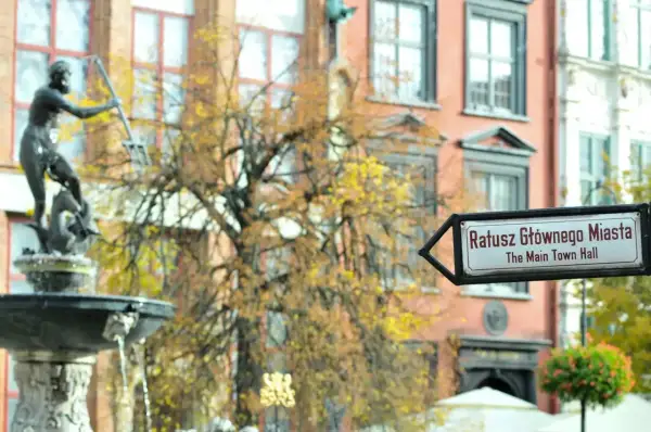 Fontanna Neptuna i drogowskaz na Ratusz Głównego Miasta w altstadt Danzig. Jesienne liście drzew tworzą tło dla zabytkowej architektury.